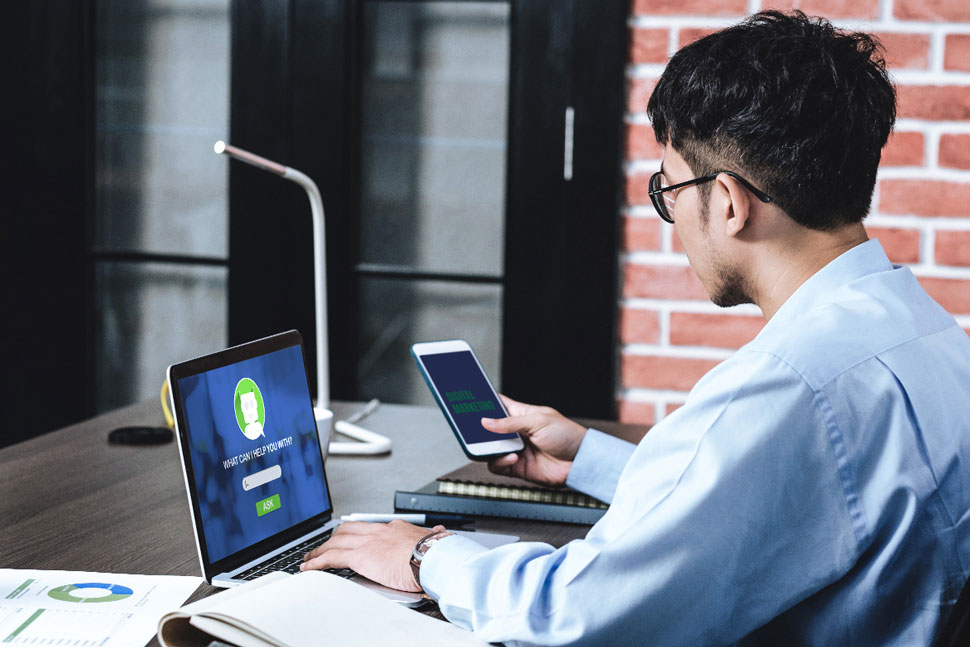 hình ảnh người đàn ông đang đang nhập chatbot trên laptop và điện thoại để chuẩn bị làm việc