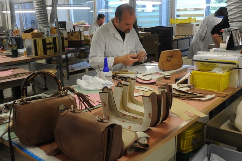 Thợ đang tiến hành may túi, trên bàn là các mảnh da để làm sản phẩm. 