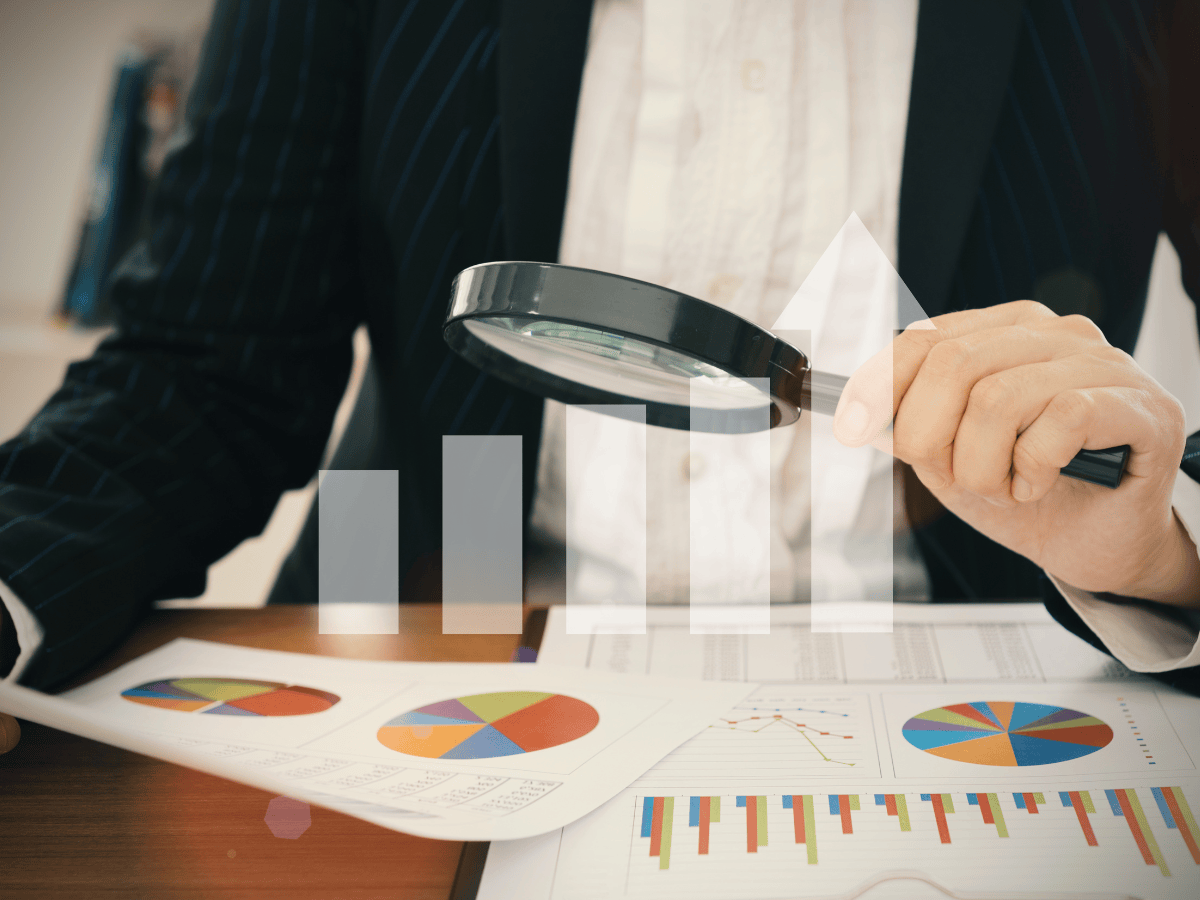 Một người đang cầm kính lúp để xem xét, so sánh biểu đồ và số liệu