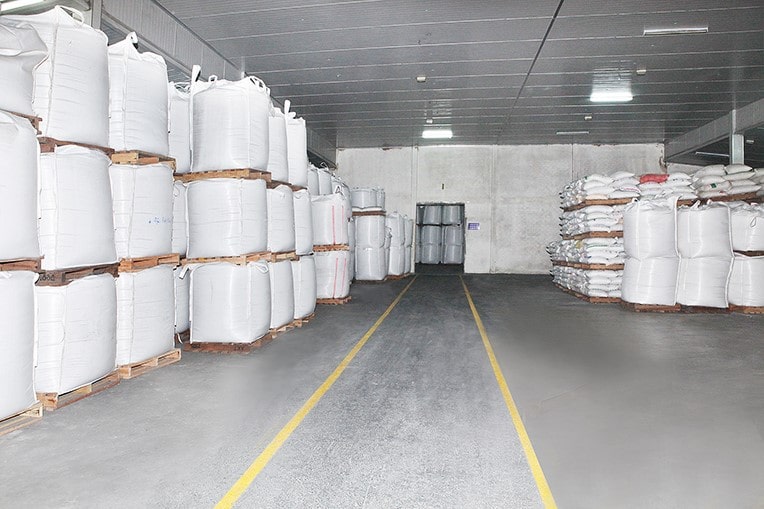 Trong kho lạnh, gạo được bảo quản trong túi rút lớn màu trắng xếp gọn gàng, ngăn nắp bên trái. Hàng đối diện là các bao gạo màu trắng xếp trên pallet gỗ