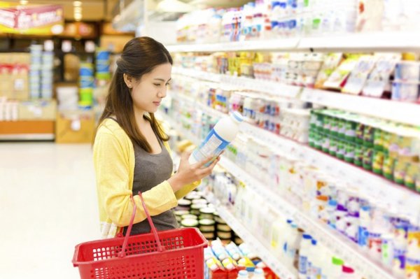 Người phụ nữ đang đứng trước kệ hàng sữa và đang xem xét, lựa chọn sản phẩm phù hợp