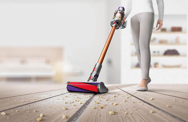 Một người đang dùng máy hút bụi để hút bụi bẩn trên mặt sàn