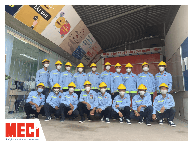 Đội ngũ nhân viên kỹ thuật tại nhà xưởng MECI: áo xanh, nón vàng, logo MECI đỏ