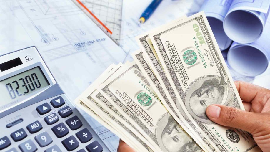 Một người đang đếm tiền, bên cạnh là máy tính và giấy tờ