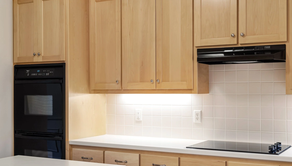 Một bàn bếp màu trắng, bên là các ngăn tủ màu nâu gỗ sáng