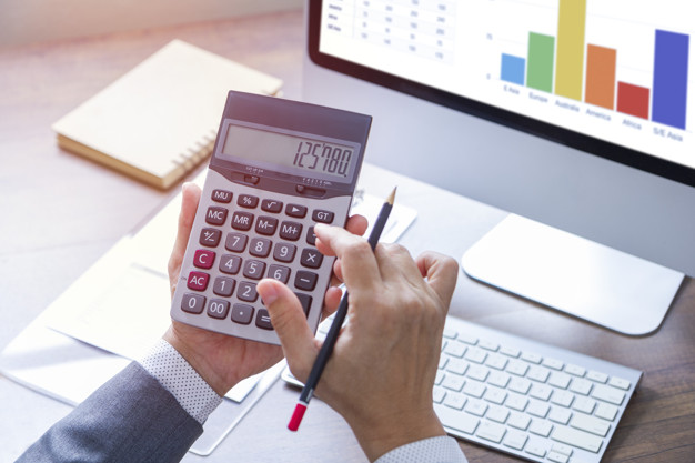 Người đàn ông đang bấm máy tính, trên bàn là máy tính và sổ sách