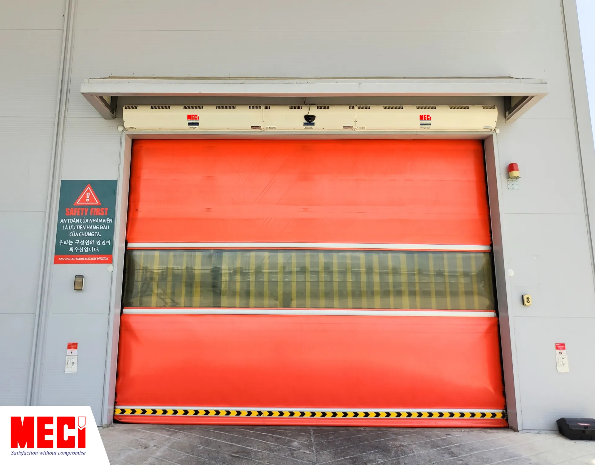 cửa cuốn nhanh pvc màu đỏ đang đóng kín ở lối vào chính 1 nhà kho có 2 quạt cắt gió phía trên