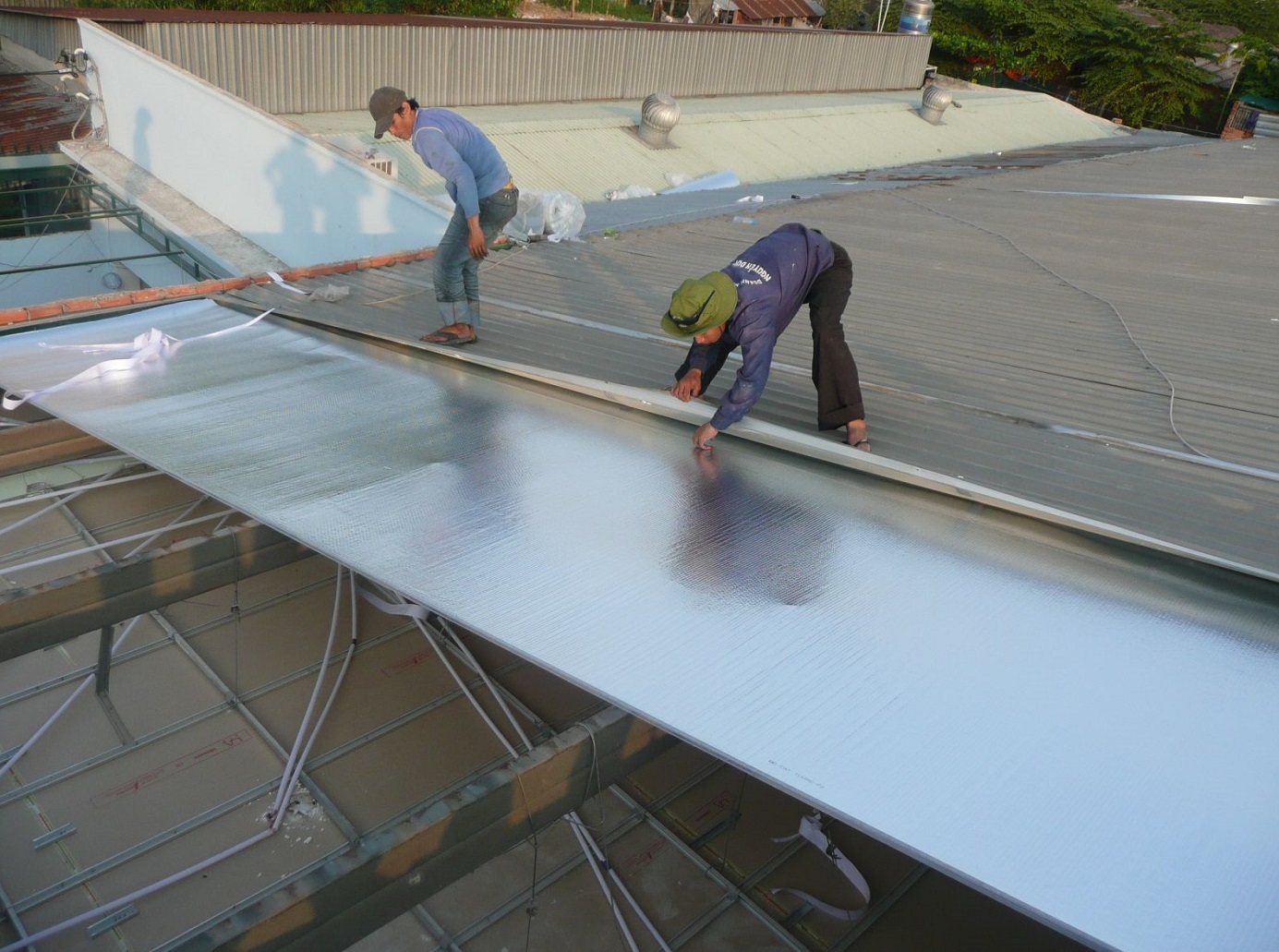 Hai người đàn ông đang lợp tấm lợp màu đen chống ồn cho mái tôn.