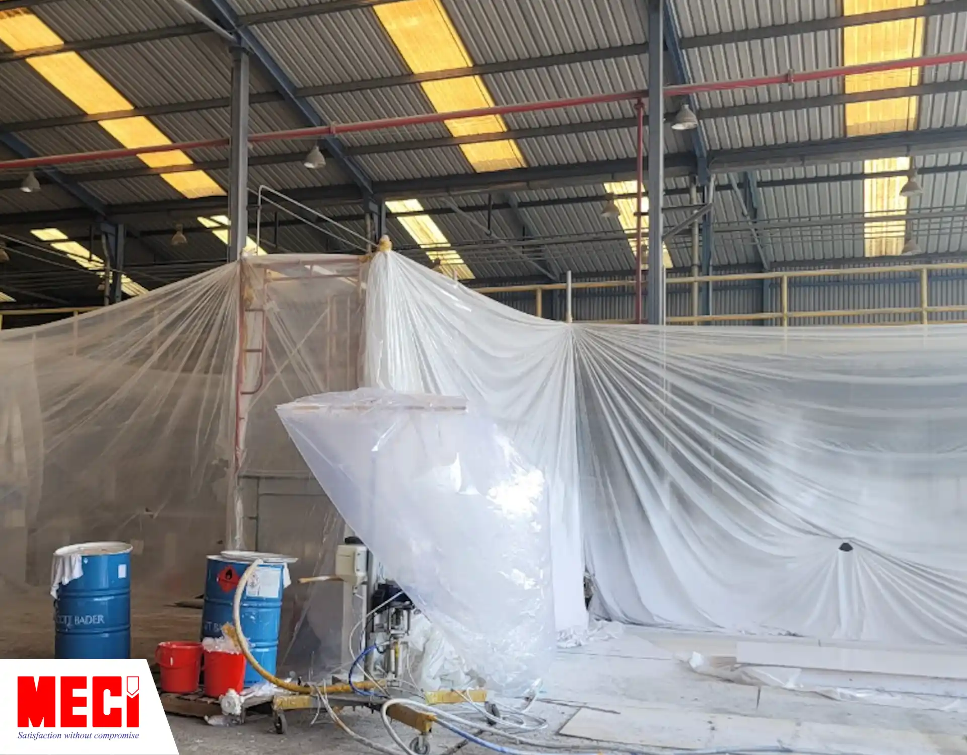 bạt nilon bao xung quanh 1 khu vực trong nhà xưởng, xung quanh có nhiều thùng sơn dầu
