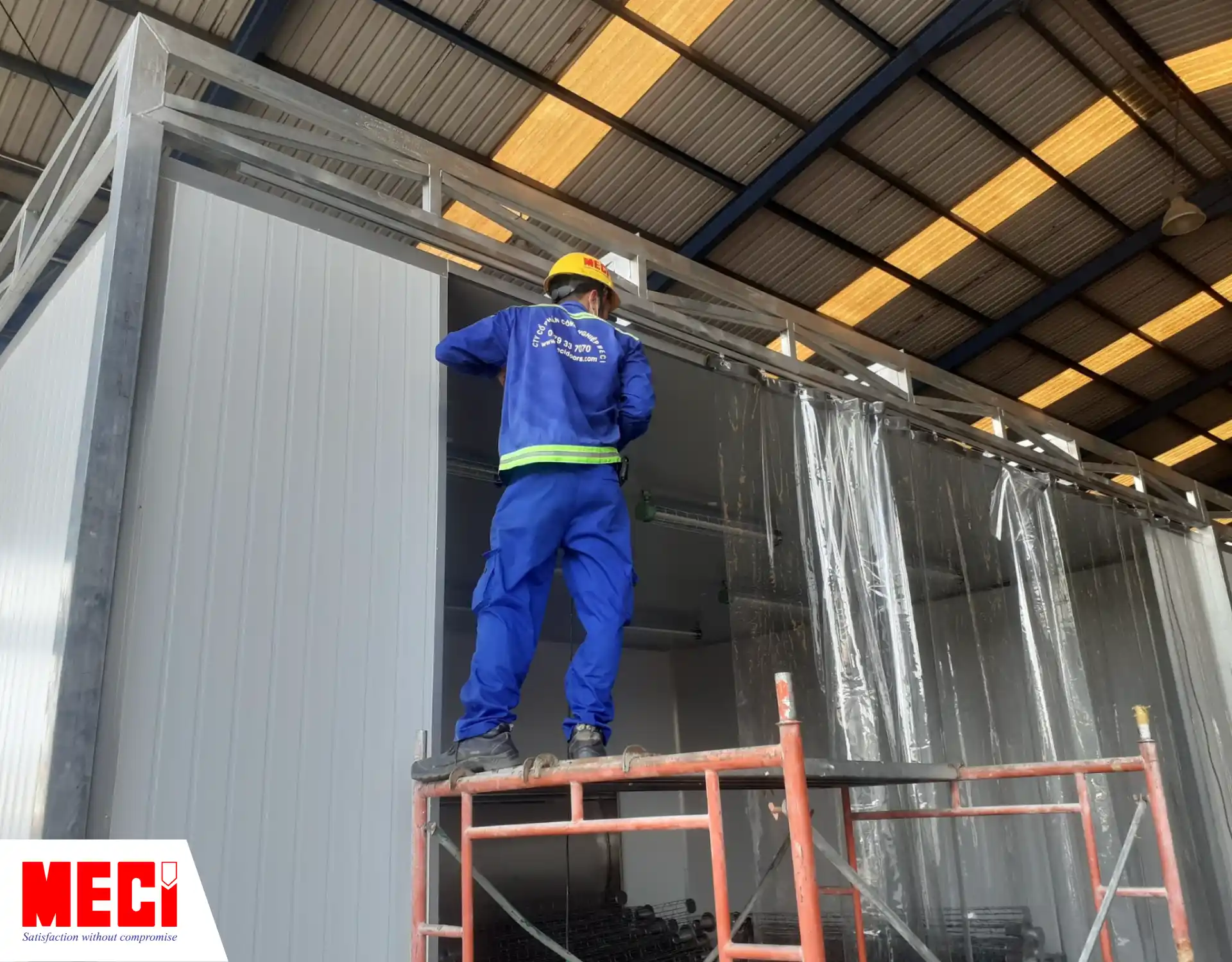 một kỹ thuật viên đang leo trên giàn giáo để lắp rèm nhựa PVC ngăn bụi cho xưởng tàu corsair marine