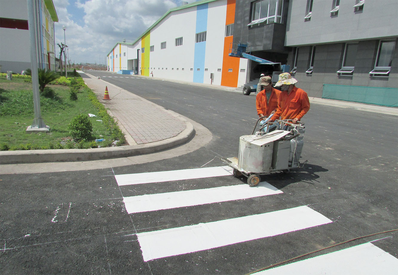 Hai nhân công đang thực hiện sơn kẻ vạch cho đường đi bên ngoài nhà xưởng