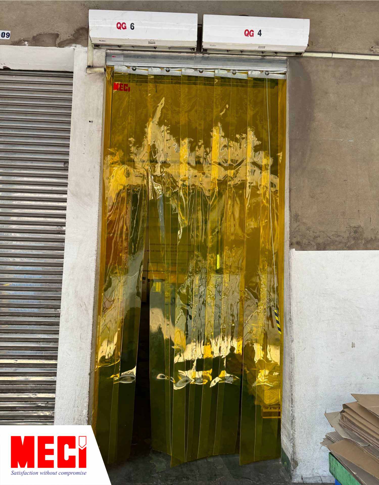 rèm nhựa PVC màu vàng hệ xếp gấp được lắp tại lối đi hẹp, phía trên có 2 quạt chiếc quạt cắt gió cạnh nhau