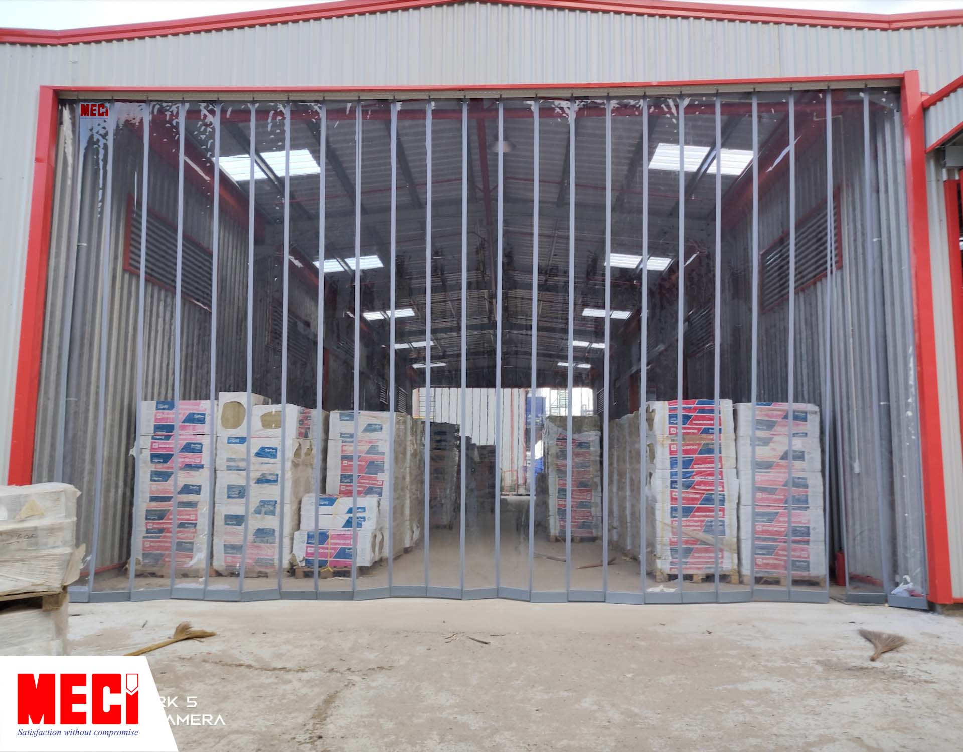 rèm nhựa PVC nam châm được lắp tại lối ra vào của một nhà kho, bên trong có nhiều thùng hàng chất chồng