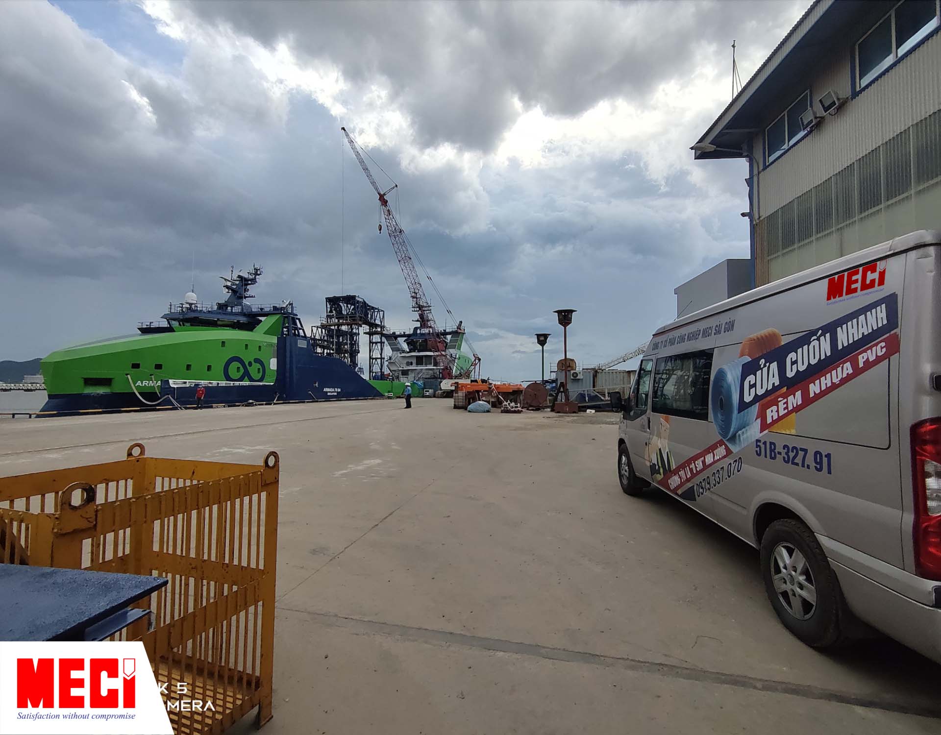 xe bán tải MECI đậu trong xưởng đóng tàu, bên trái là 1 con tàu lớn đang được đóng trên biển