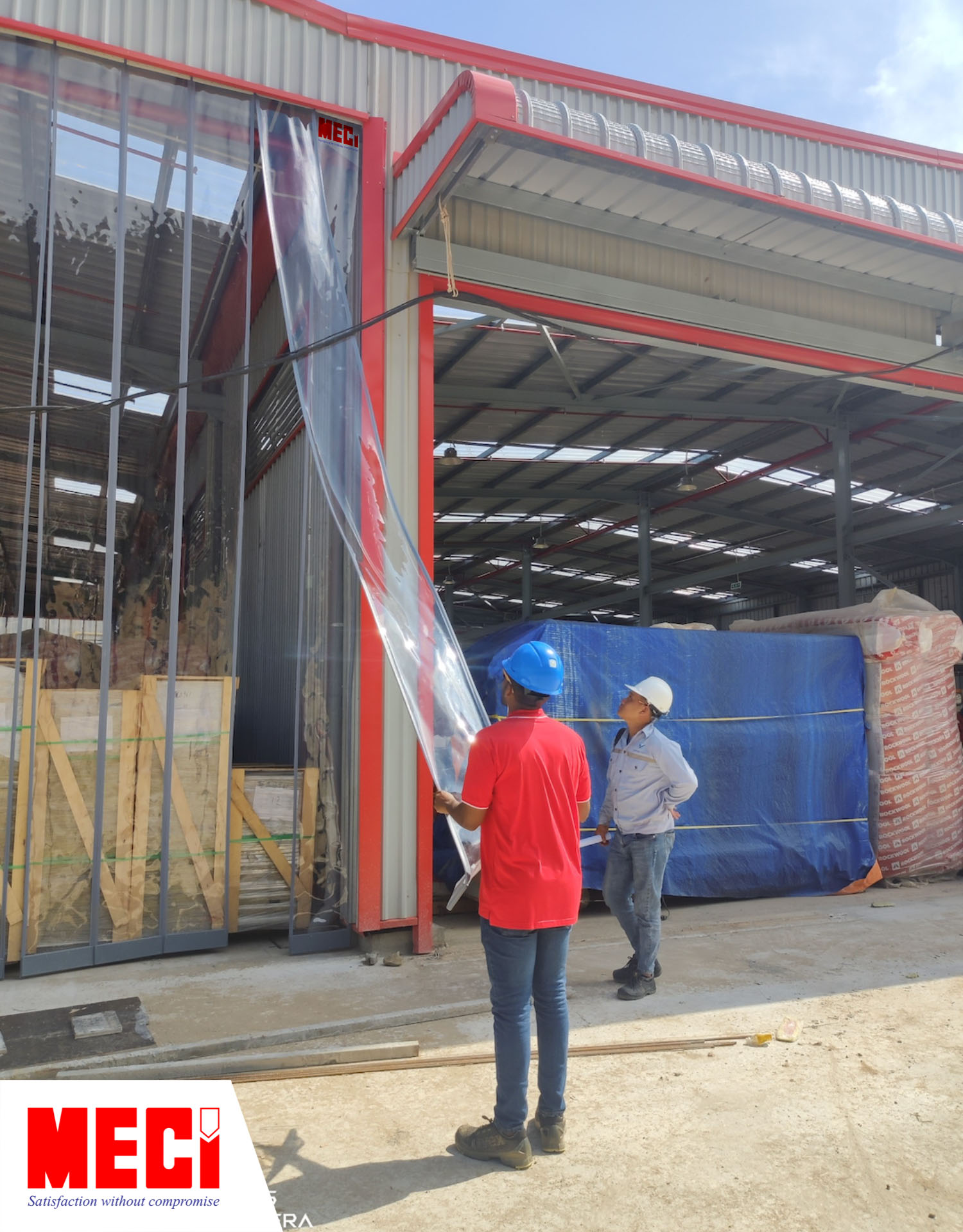 một người đàn ông đang kéo sợi rèm nam châm tại xưởng đóng tàu VARD Vũng Tàu, người còn lại nhìn tấm rèm nhựa PVC nam châm được lắp tại lối vào