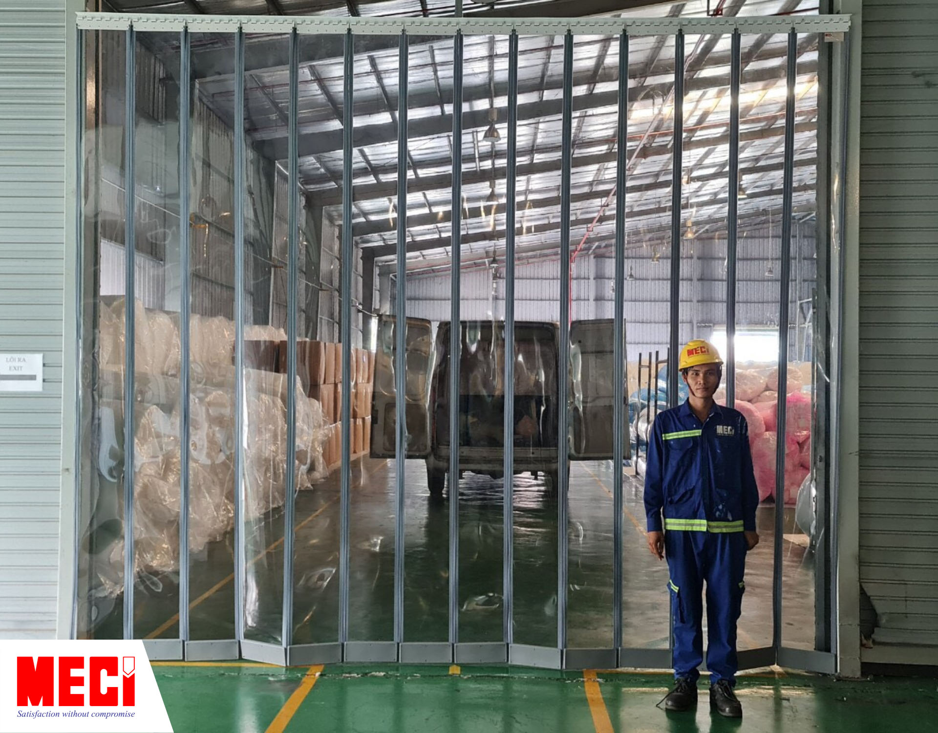 một người mặc đồ kỹ thuật đứng trước rèm nhựa nam châm, phía sau rèm là khu vực kho