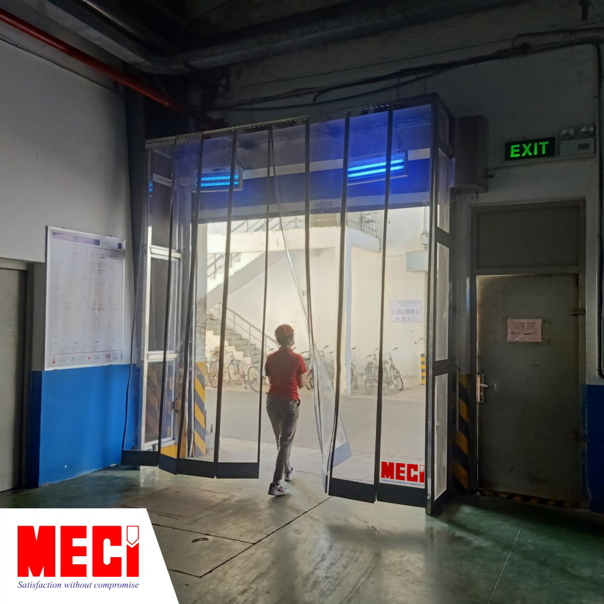 một người phụ nữa đi qua cái rèm, ảnh chụp từ bên trong nhà xưởng thể hiện rèm nhựa nam châm thuận tiện đi lại