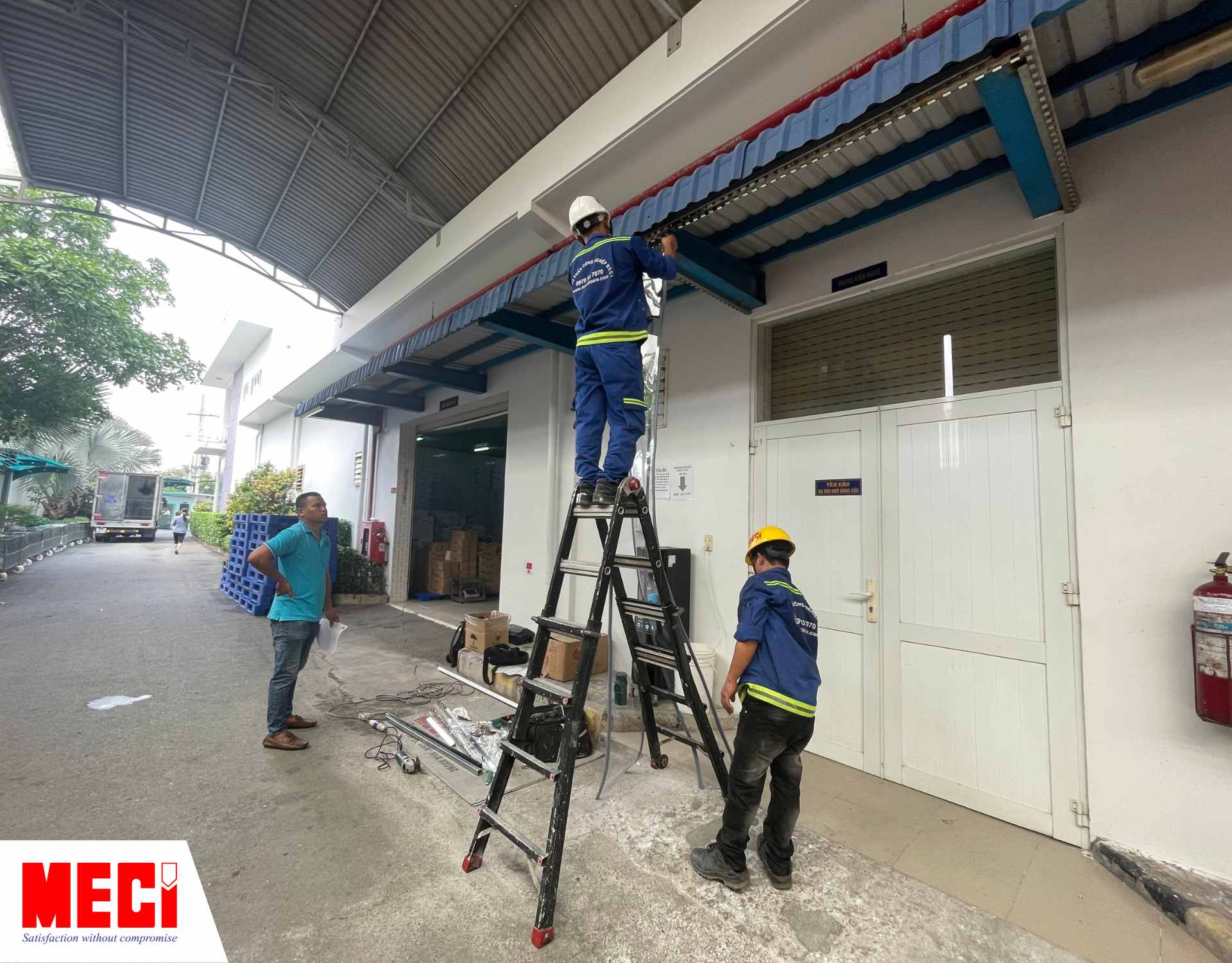 một người nam đang trèo lên thang treo sợi nhựa nam châm lên, hai người bên dưới đứng nhìn