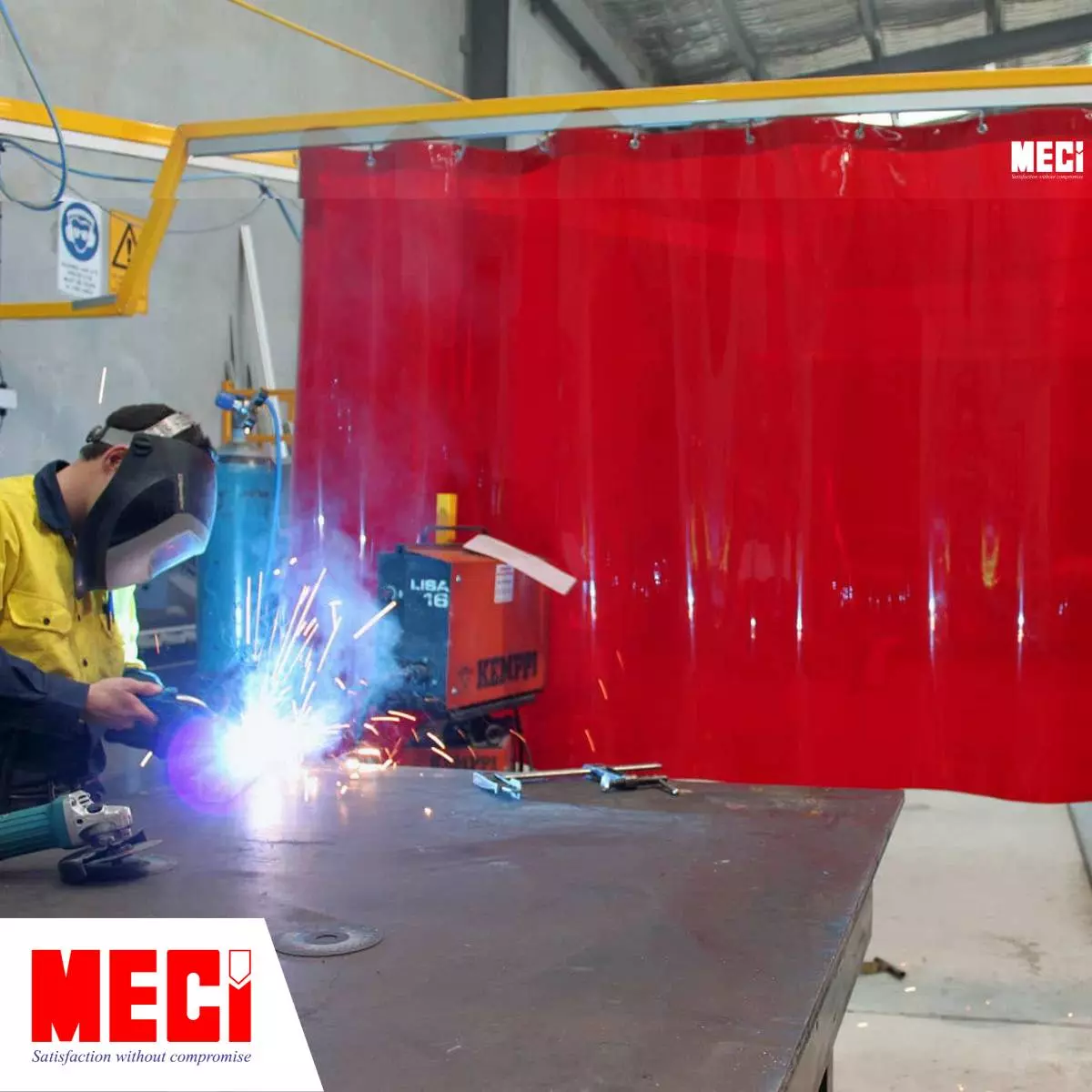 một người đàn ông đang hàn cắt kim loại phía sau một tấm rèm kéo dạt màu đỏ, tia lửa hàn chói loá bắn vào tấm màn