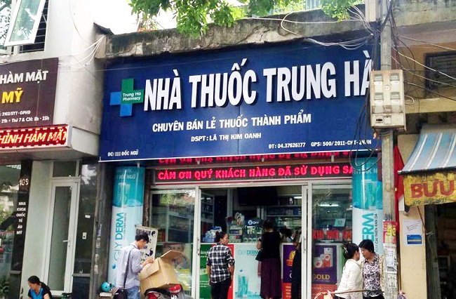 Một bảng hiệu quầy thuốc được gắn trên nhà thuốc, trước quầy có nhiều người mua thuốc