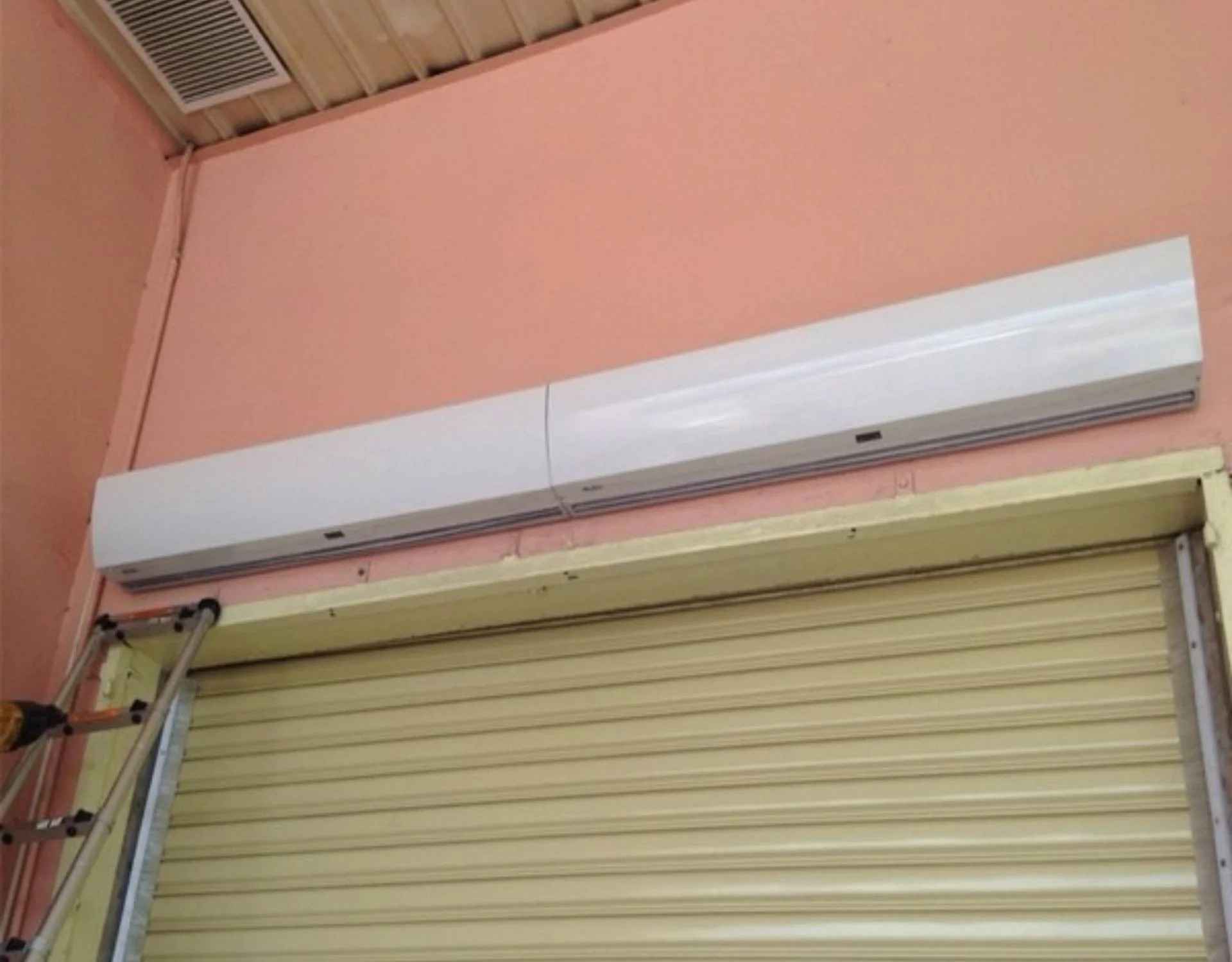 hai chiếc quạt cắt gío nedfon được lắp cạnh nhau, cố định mặt lưng vào vách tường màu hồng, bên dưới là cửa cuốn nan nhôm đang đóng xuống