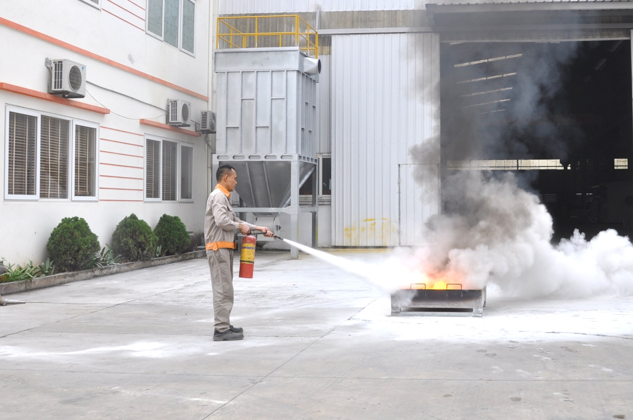 Một người đàn ông đang dùng bình chữa cháy xịt vào vùng cháy ở trước một phân xưởng.