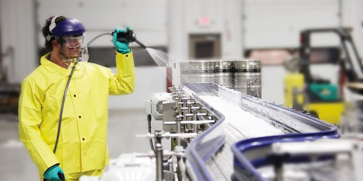 Một nhân viên vệ sinh mặc đồ bảo hộ đang vệ sinh dây chuyền sản xuất.