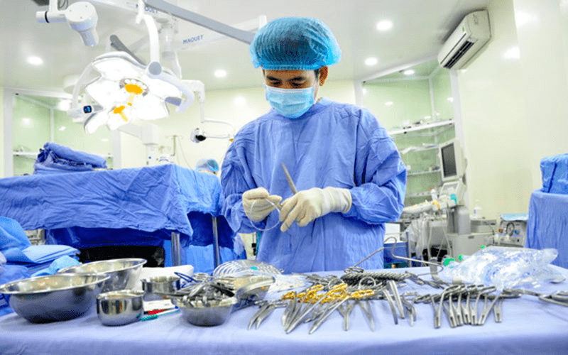 Bên trong một phòng mổ, có nhân viên y tế đang chuẩn bị dụng cụ mổ