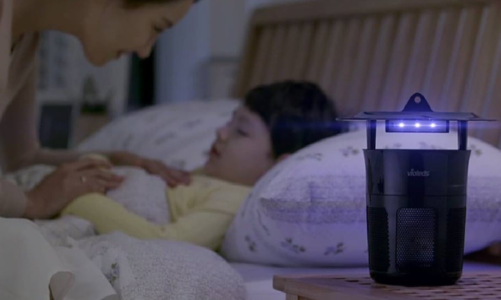 cái đèn bắt muỗi đặt trên bàn phía sau có một người mẹ đang cho con ngủ