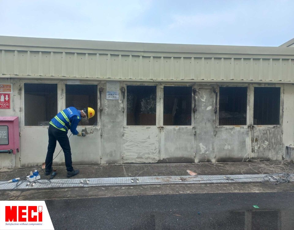 một người đàn ông đang mài lớp sơn bên ngoài căn nhà