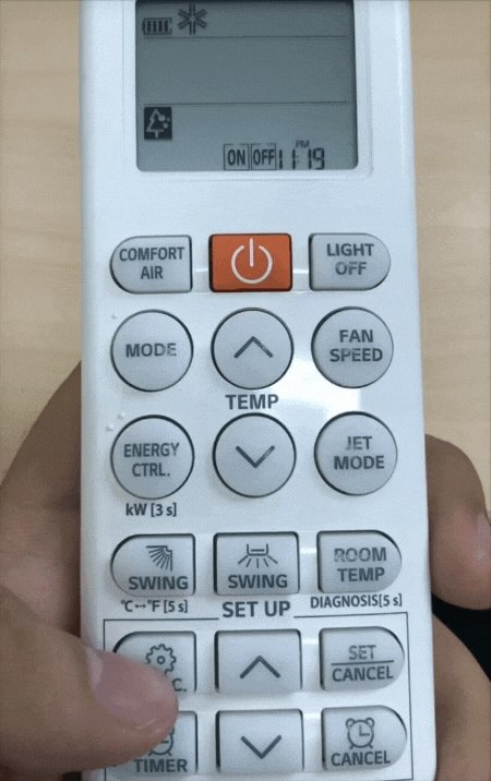 một bàn tay đan ấn nút trên remote máy lạnh