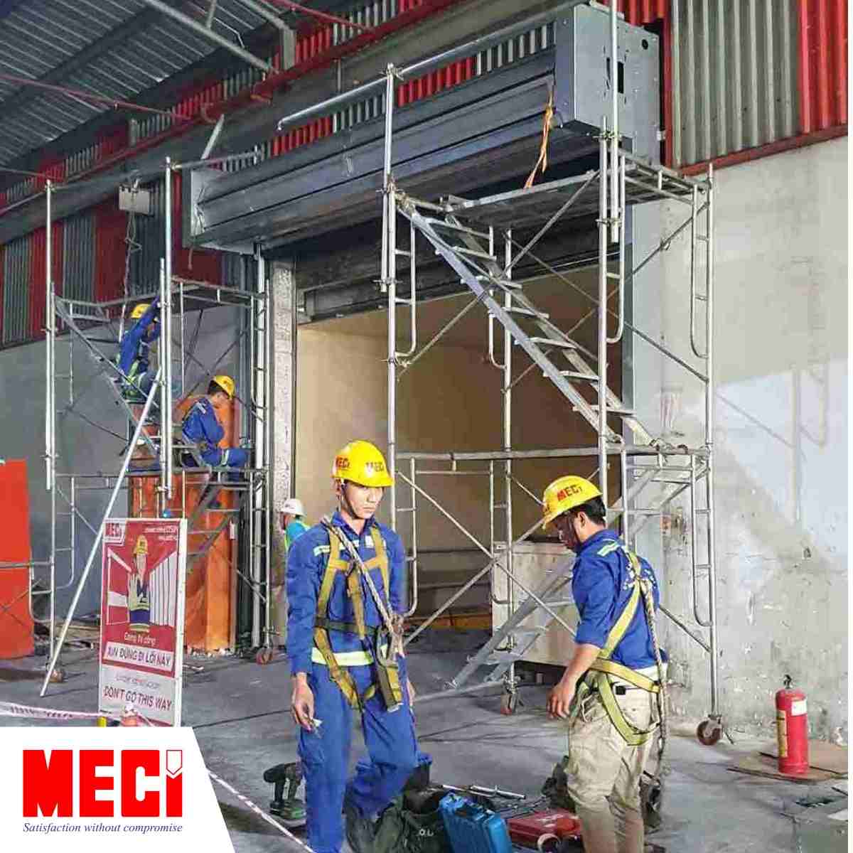 Kỹ thuật MECI đeo dây bảo hộ, xung quanh có dàn giáo và biển báo của MECI