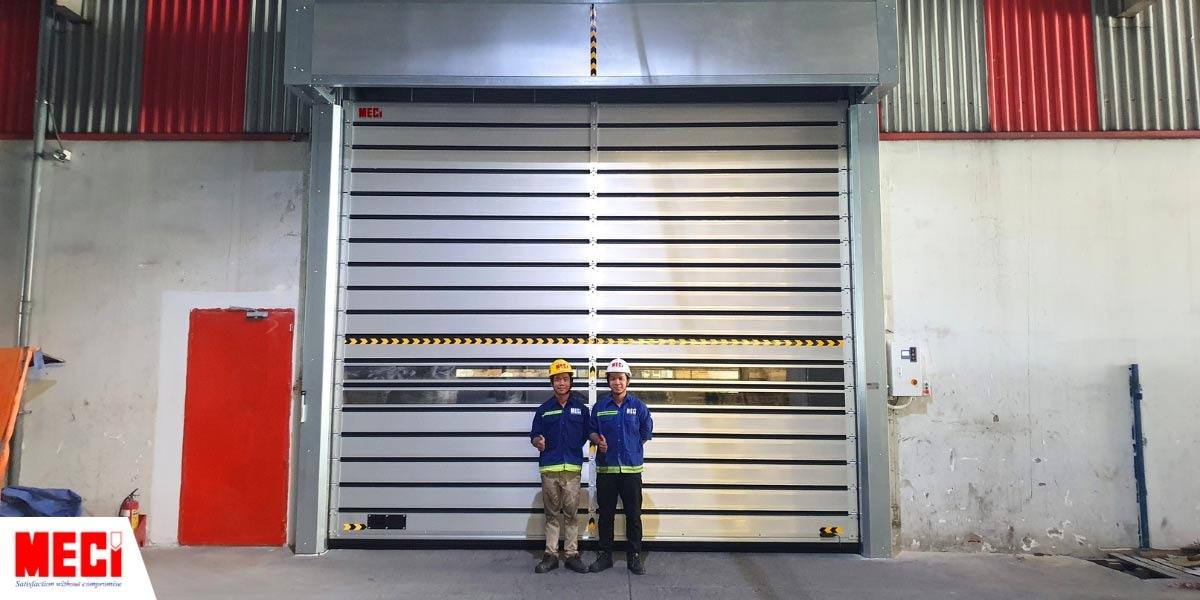 2 kỹ thuận MECI đứng trước cửa cuốn nhanh nan nhôm