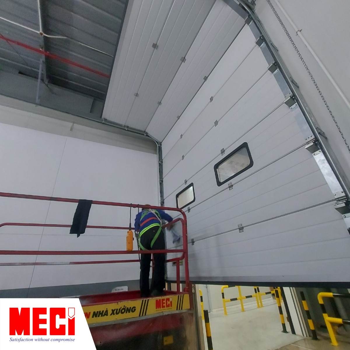 một kỹ thuật đang đứng trên thang nâng tự động kiểm tra ray dẫn và con lăn của cửa trượt trần