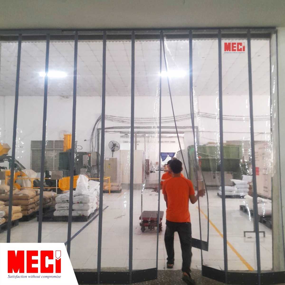 Một người mặc áo cam đang dùng tay đẩy rèm nhựa nam châm để đi qua